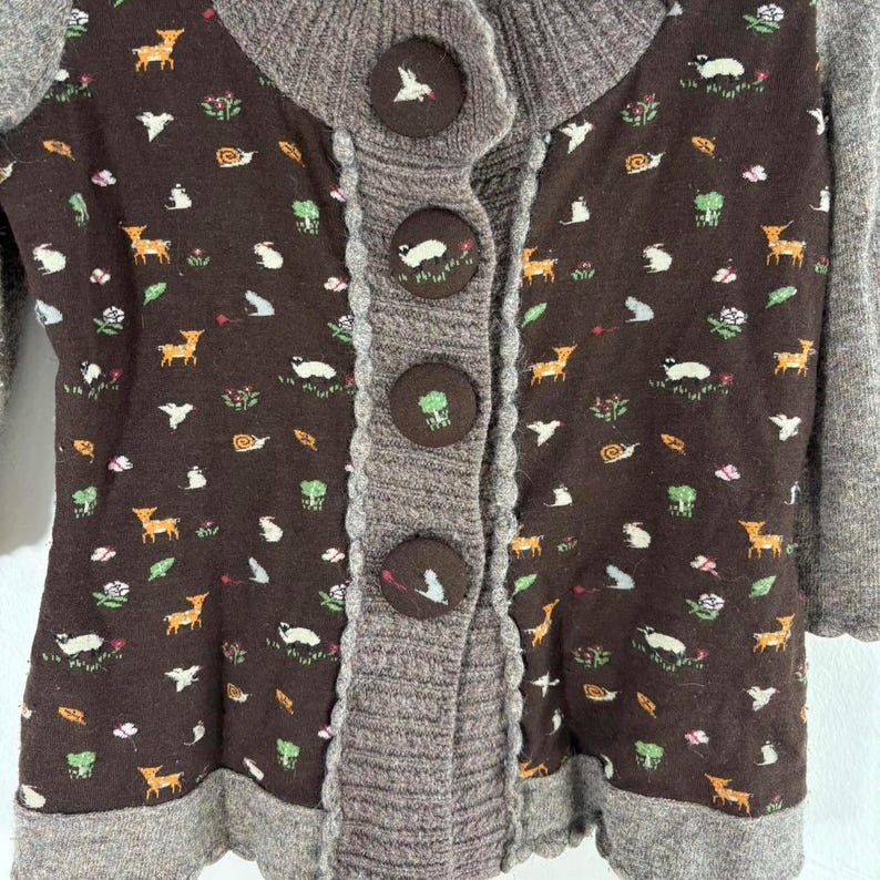 May include: A brown cardigan with a gray knit trim and a pattern of small animals and plants. The cardigan has five large buttons.