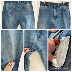 May include: Light blue denim Wrangler jeans with a classic five-pocket design. Features a worn look with distressed areas and a leather patch on the back pocket. The jeans have a button and zipper closure.