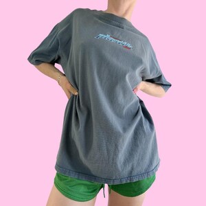 May include: A dark blue oversized t-shirt with the word "Plastik" printed on the front in a blue, red, and white graphic font.
