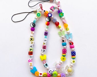 May include: Two colorful beaded phone straps with pearl beads, charms, and letter beads spelling out the names "Ariana" and "Kayleigh".