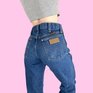 May include: A pair of blue denim jeans with a brown leather patch on the back pocket that says "Wrangler".