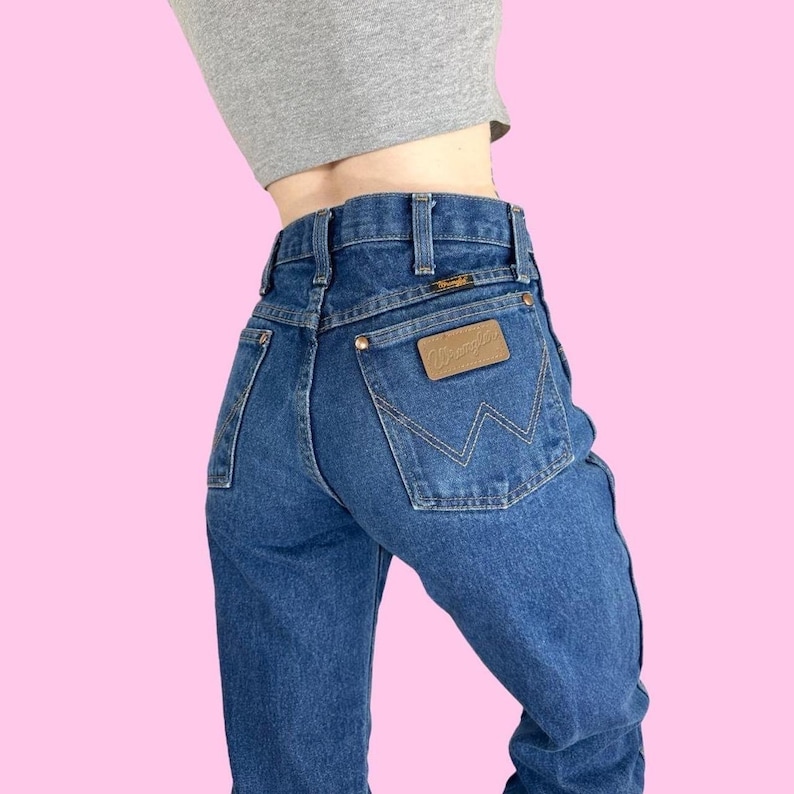 May include: A pair of blue denim jeans with a brown leather patch on the back pocket that says "Wrangler".