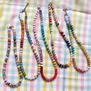 May include: Six colorful beaded necklaces with various bead shapes and sizes. The necklaces feature a variety of colors, including red, yellow, green, blue, and pink. Each necklace has a silver clasp.