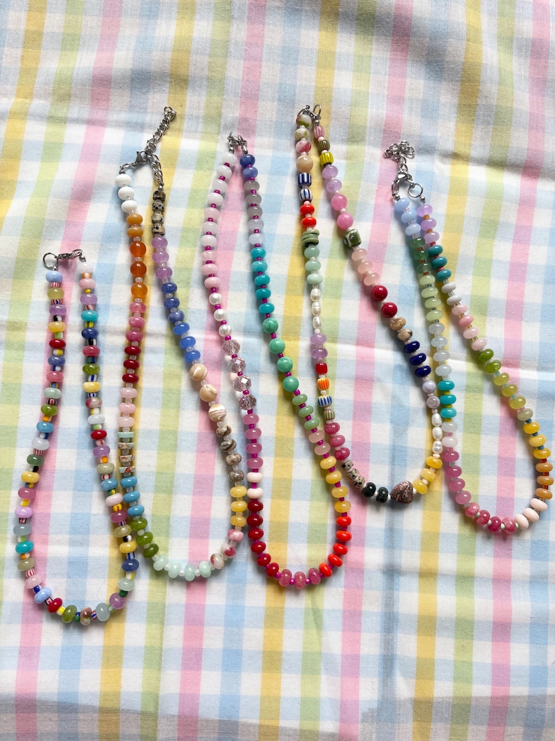 May include: Six colorful beaded necklaces with various bead shapes and sizes. The necklaces feature a variety of colors, including red, yellow, green, blue, and pink. Each necklace has a silver clasp.