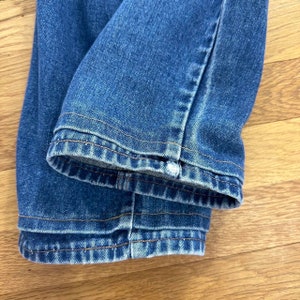Puede incluir: Primer plano del dobladillo de un par de pantalones vaqueros de mezclilla azul. Los vaqueros est&aacute;n doblados y las costuras son visibles.