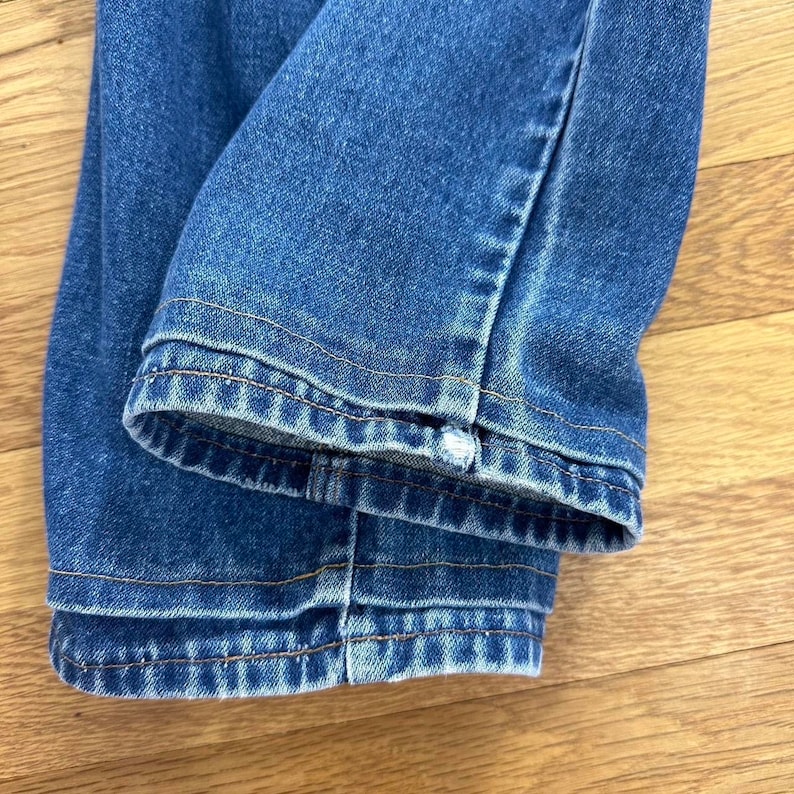 Puede incluir: Primer plano del dobladillo de un par de pantalones vaqueros de mezclilla azul. Los vaqueros est&aacute;n doblados y las costuras son visibles.