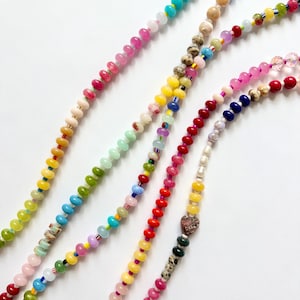 May include: Close-up of several beaded necklaces in various colors, including pink, yellow, green, and blue. The beads are small and round, strung together to create a colorful and eye-catching accessory. The necklaces are displayed against a white background.