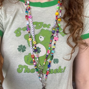 May include: A multi-colored beaded necklace with a charm of a Care Bear and the words "I've got the luck!"  The necklace has a silver key chain attached to it.
