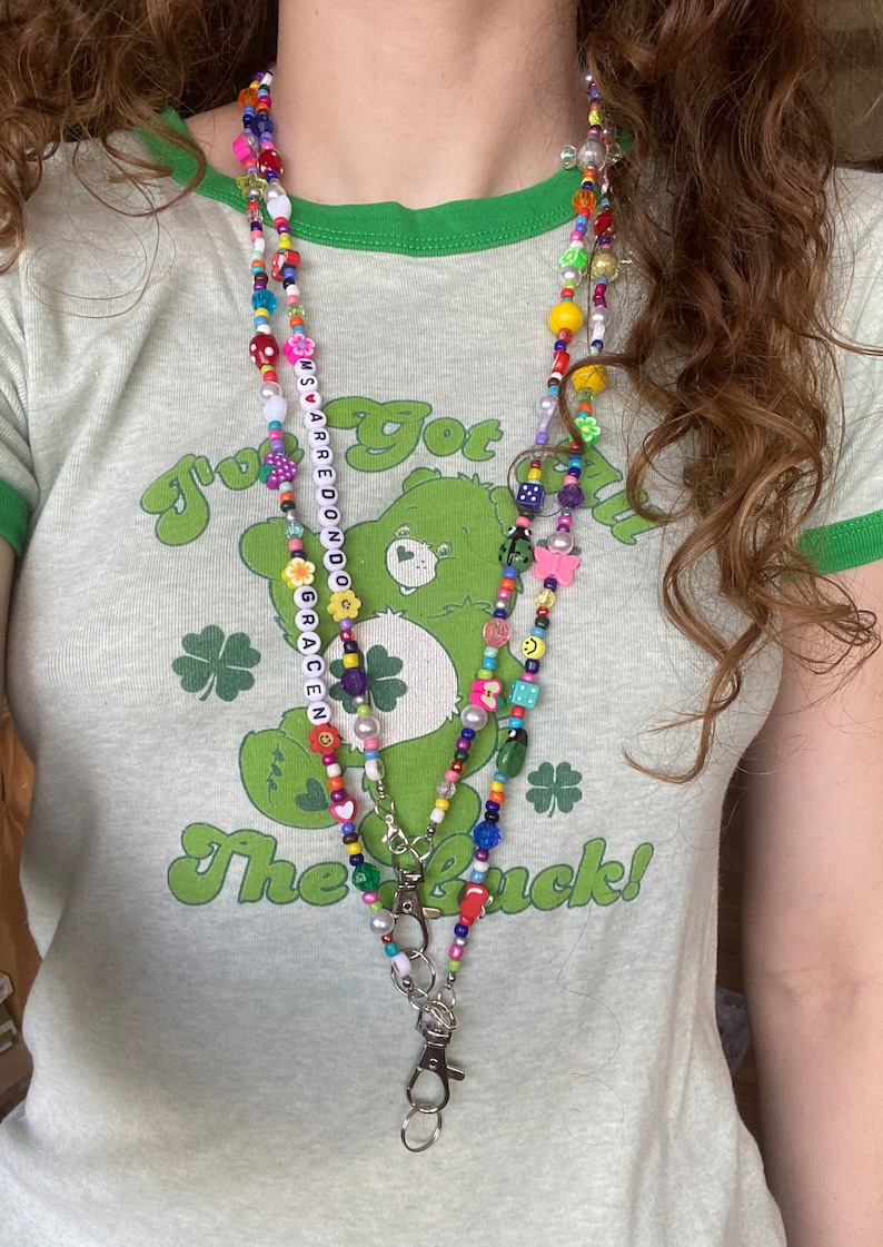 May include: A multi-colored beaded necklace with a charm of a Care Bear and the words "I've got the luck!"  The necklace has a silver key chain attached to it.