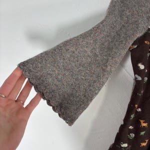 May include: A brown sweater with a scalloped edge and a brown and white patterned fabric underneath.