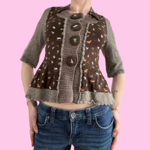 May include: A brown cardigan with a brown and white floral pattern and a ruffled hem. The cardigan has a button closure and is made of a soft, knitted fabric.