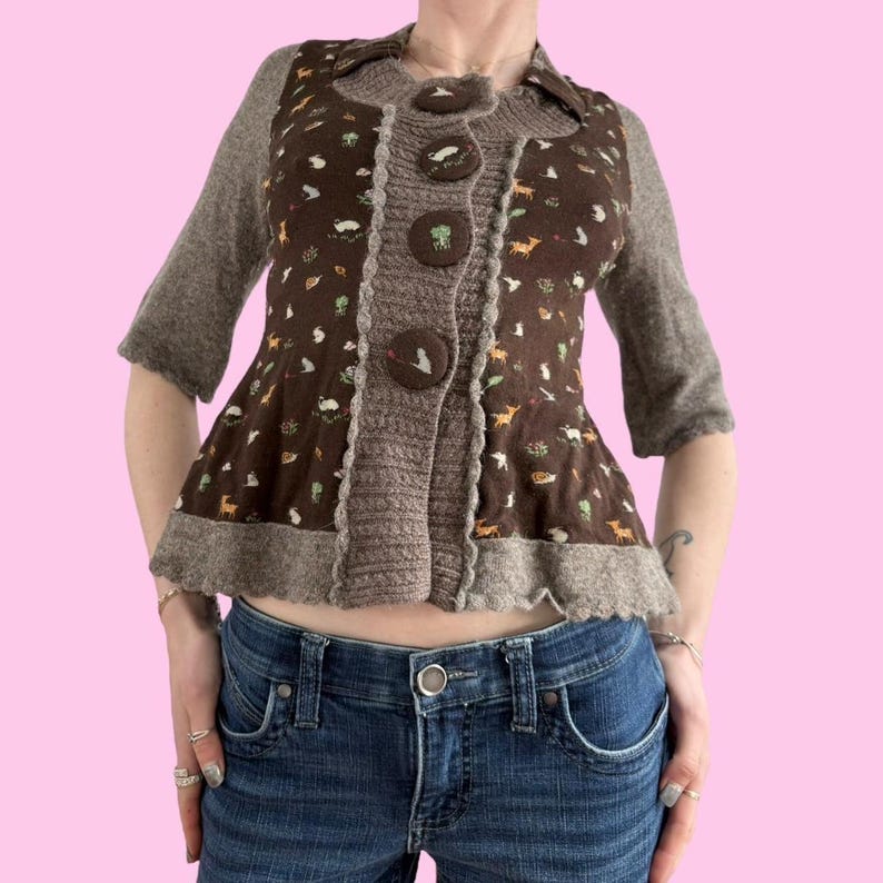 May include: A brown cardigan with a brown and white floral pattern and a ruffled hem. The cardigan has a button closure and is made of a soft, knitted fabric.