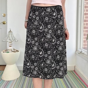 May include: A black and white floral print skirt. The skirt features a black background with a white floral pattern. The skirt has a black waistband and hemline. The skirt is knee-length and appears to be made of a lightweight fabric.