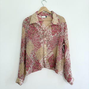 May include: A long-sleeved, button-up shirt with a floral print in shades of pink and beige. The shirt has a collared neckline and a relaxed fit.
