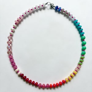 May include: A colorful beaded necklace with a variety of round beads in a rainbow of colors, including pink, red, yellow, green, and blue. The beads are strung on a pink cord and secured with a silver clasp. A unique piece of jewelry.