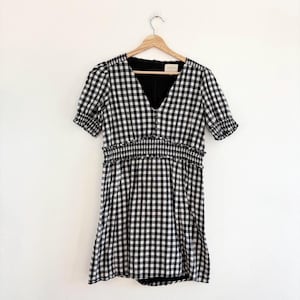 May include: Black and white gingham dress with short sleeves and a v-neck. The dress has a smocked waist and a slightly flared skirt.