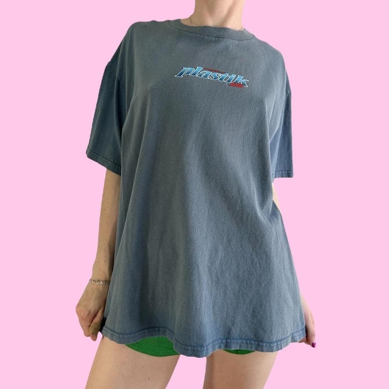 May include: A dark blue t-shirt with a white, blue, and red "Plastik 2000" graphic on the front.