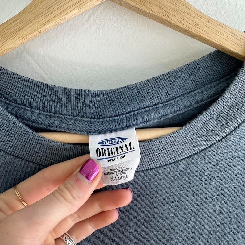 May include: A gray T-shirt with a white tag that reads "TULTEX ORIGINAL PRESHRUNK 100% COTTON ASSEMBLED IN MEXICO OF U.S.A. PARTS X-Large"
