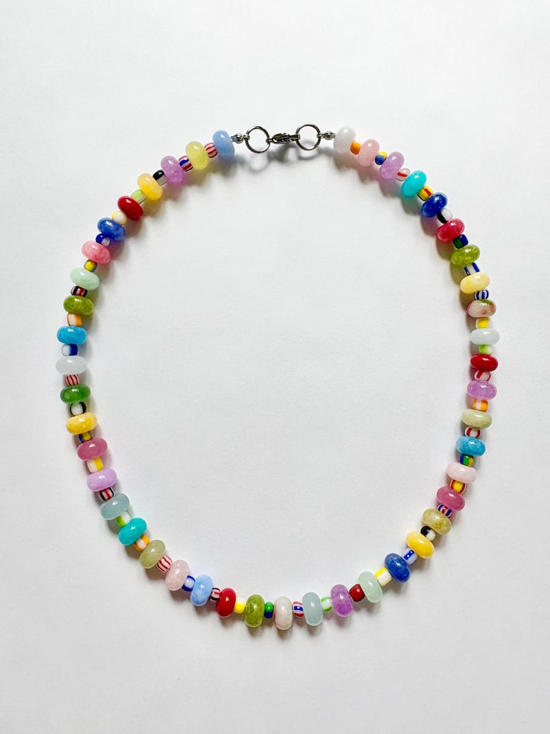 May include: A colorful beaded necklace with a variety of small, round beads in shades of red, yellow, green, blue, pink, and purple. The necklace has a silver-colored clasp and is displayed against a white background. The beads are approximately 0.25 inches in diameter.