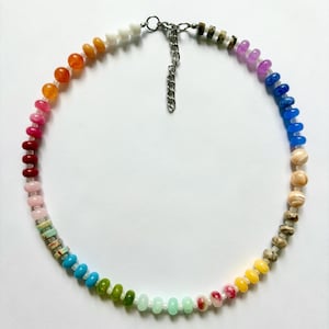 May include: A colorful beaded necklace featuring a rainbow of hues. The necklace showcases a variety of small, round beads in shades of red, orange, yellow, green, blue, and purple. The necklace has a silver-toned chain and clasp.