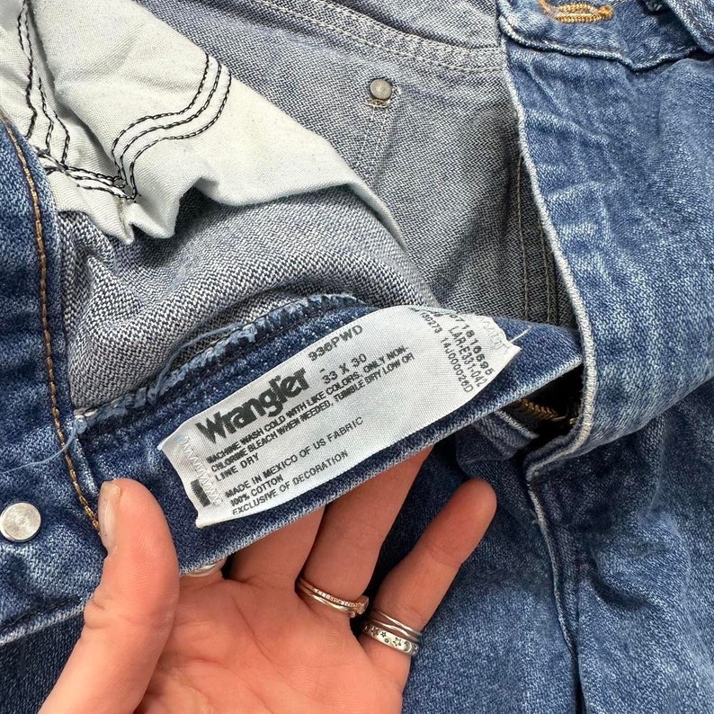May include: Close-up of a pair of Wrangler blue denim jeans. The jeans have a tag that reads "Wrangler 33 x 30". The jeans are made of 100% cotton and are made in Mexico.