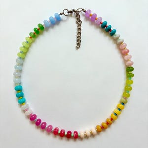 May include: A colorful beaded necklace with a rainbow gradient of colors. The necklace features small, round beads in shades of pink, red, yellow, green, blue, and purple. It has a silver-tone clasp and chain for adjustable length.