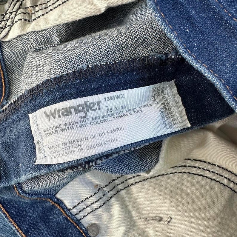May include: Blue denim jeans with a white care label that reads "Wrangler 13MWZ 35 X 30 Machine Wash Hot and Inside Out First Three Times With Like Colors, Tumble Dry Made in Mexico of US Fabric 100% Cotton Exclusive of Decoration"