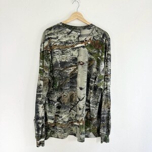 May include: A long-sleeved shirt with a camouflage pattern in shades of green, brown, and white. The shirt has a crew neck and a relaxed fit.