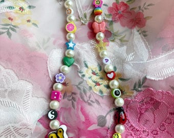 May include: A white pearl necklace with colorful plastic charms, including butterflies, stars, hearts, smiley faces, and a yin yang symbol.