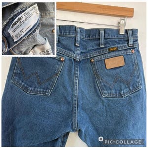 May include: Close-up of the back of blue denim Wrangler jeans. The jeans have two back pockets with the Wrangler logo stitched on them. A leather patch with the Wrangler logo is centered above the right pocket. The jeans are size 32x30.