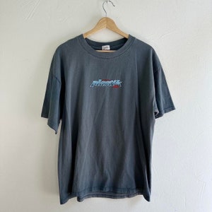 May include: A dark gray t-shirt with a blue and red embroidered logo that says "plastik" on the front.