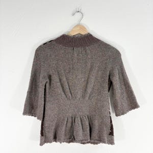 May include: A brown sweater with a ruffled hem and a high neckline. The sweater is made of a soft, knit fabric.