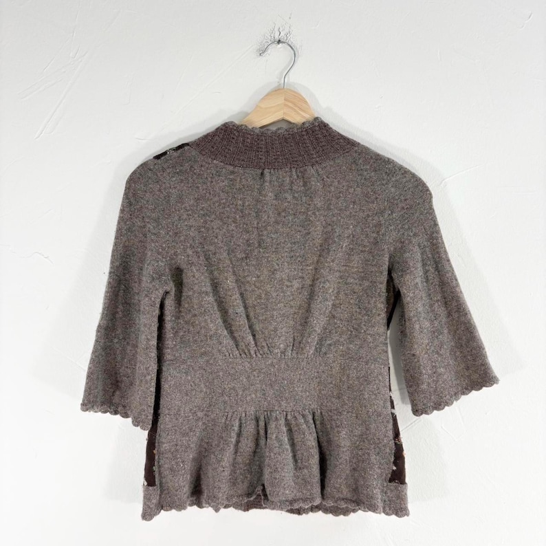 May include: A brown sweater with a ruffled hem and a high neckline. The sweater is made of a soft, knit fabric.