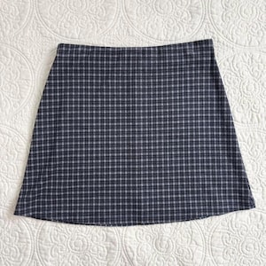Puede incluir: Falda de l&iacute;nea A con estampado de cuadros azul marino y blanco. La falda tiene un dise&ntilde;o cl&aacute;sico, con un dobladillo recto. La tela parece ser un material tejido, adecuado para varias estaciones. Una pieza vers&aacute;til para un armario casual o semiformal.