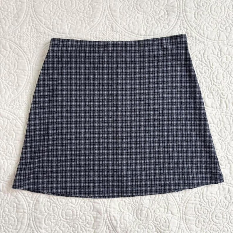 Puede incluir: Falda de l&iacute;nea A con estampado de cuadros azul marino y blanco. La falda tiene un dise&ntilde;o cl&aacute;sico, con un dobladillo recto. La tela parece ser un material tejido, adecuado para varias estaciones. Una pieza vers&aacute;til para un armario casual o semiformal.