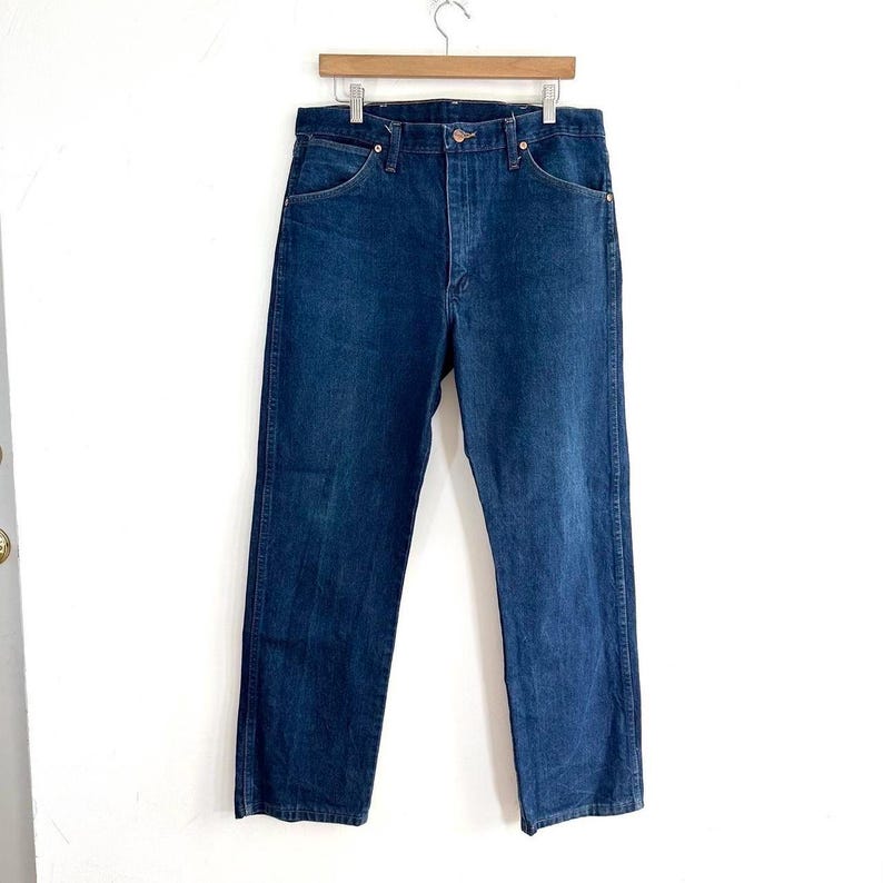 May include: A pair of dark blue denim jeans with a button fly and five pockets.