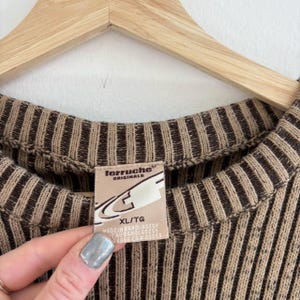 Pode incluir: Camisola de malha com riscas castanhas e bege com uma etiqueta castanha que diz "ferruche originals" e "XL/TG". A etiqueta tamb&eacute;m diz "Made in Bangladesh" e "100% algod&atilde;o".