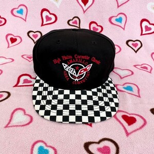 May include: Black and white checkered baseball cap with a black crown and a red, white, and blue embroidered logo that reads "High Plains Corvette Classic Amarillo Area Texas Corvettes".