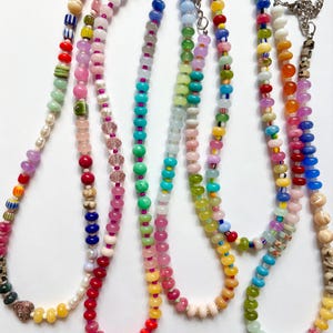 May include: A collection of colorful beaded necklaces. Each necklace features a unique combination of beads in various shapes, sizes, and colors, including pink, blue, green, yellow, and red. The necklaces have silver clasps and are displayed against a white background.