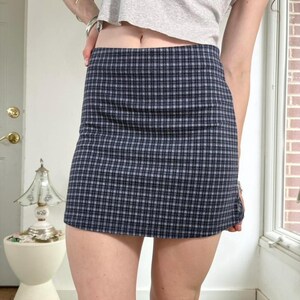 Puede incluir: Minifalda con un cl&aacute;sico estampado de cuadros en tonos azul marino, gris y blanco. La falda tiene una silueta recta y ajustada, con un dobladillo corto. La tela parece ser un material tejido, adecuado para ropa casual.