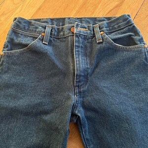 May include: A pair of dark blue denim jeans with a classic five-pocket style. The jeans have a straight leg and a button fly.