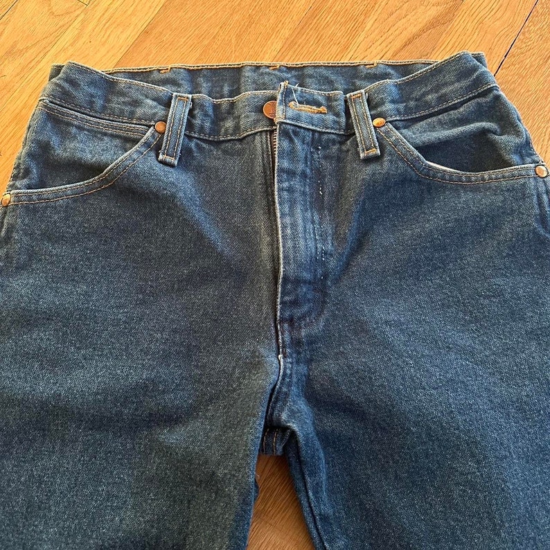 May include: A pair of dark blue denim jeans with a classic five-pocket style. The jeans have a straight leg and a button fly.