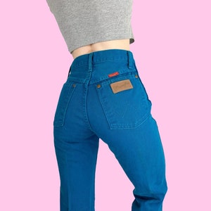Może przedstawiać: Dżinsy w kolorze niebieskim z brązową sk&oacute;rzaną naszywką z napisem "Wrangler" na tylnej kieszeni.