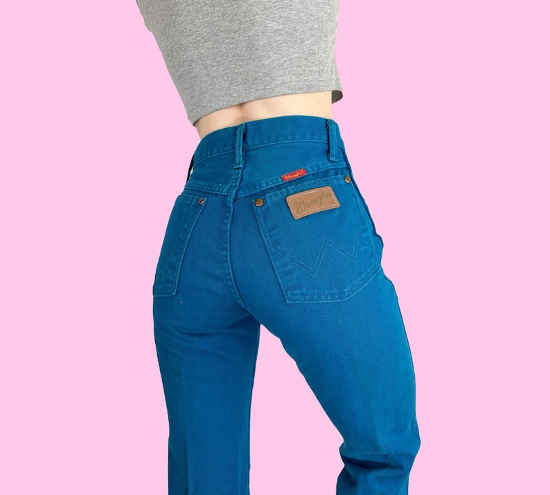 Może przedstawiać: Dżinsy w kolorze niebieskim z brązową sk&oacute;rzaną naszywką z napisem "Wrangler" na tylnej kieszeni.