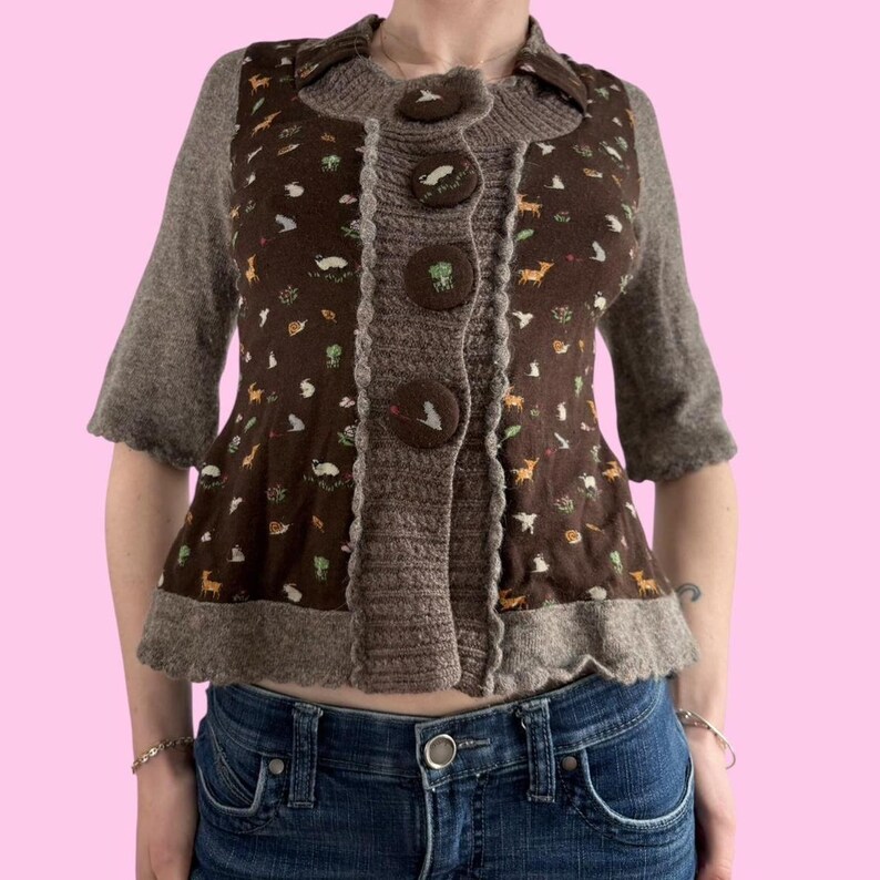 May include: A brown cardigan with a brown and white floral print and a ruffled hem. The cardigan has a button closure and is made of a soft, knitted fabric.