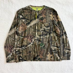 K&ouml;nnte beinhalten: Lang&auml;rmeliges Camouflage-Hemd mit Knopfleiste. Das Hemd hat ein Muster aus braunem, gr&uuml;nem und beigem Laub. Der Kragen und die Innenseite der Knopfleiste sind leuchtend neongelb. Das Hemd ist aus leichtem Material gefertigt.
