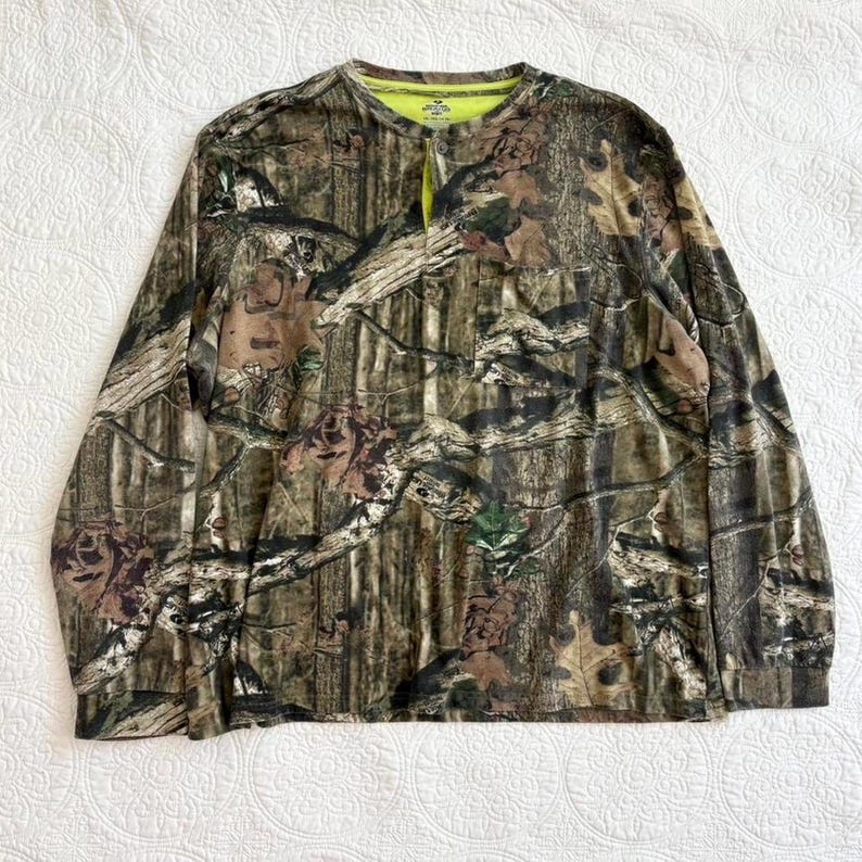 K&ouml;nnte beinhalten: Lang&auml;rmeliges Camouflage-Hemd mit Knopfleiste. Das Hemd hat ein Muster aus braunem, gr&uuml;nem und beigem Laub. Der Kragen und die Innenseite der Knopfleiste sind leuchtend neongelb. Das Hemd ist aus leichtem Material gefertigt.
