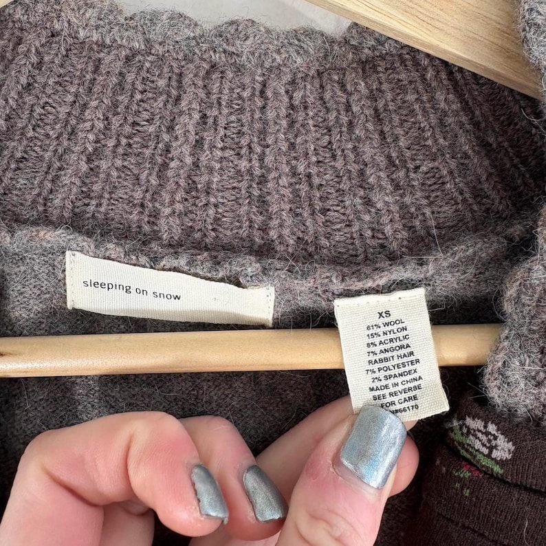 May include: A brown sweater with a tag that reads "sleeping on snow" and a smaller tag that lists the fabric composition and size as "XS". The fabric composition is 61% wool, 15% nylon, 8% acrylic, 7% angora rabbit hair, 7% polyester, and 2% spandex. The sweater is made in China.