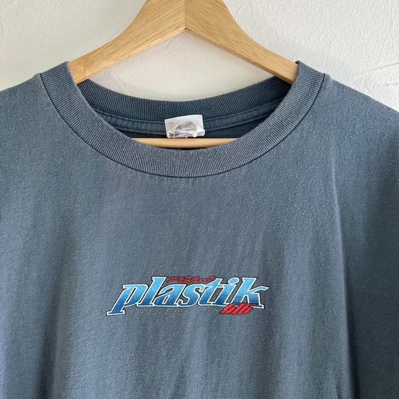 May include: A blue t-shirt with a faded blue and red graphic of the word "plastik" with Japanese text above it.