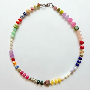 May include: A colorful beaded necklace featuring a variety of shapes and sizes. The necklace includes beads in shades of pink, red, yellow, blue, green, and white, with a heart-shaped bead and a silver clasp.